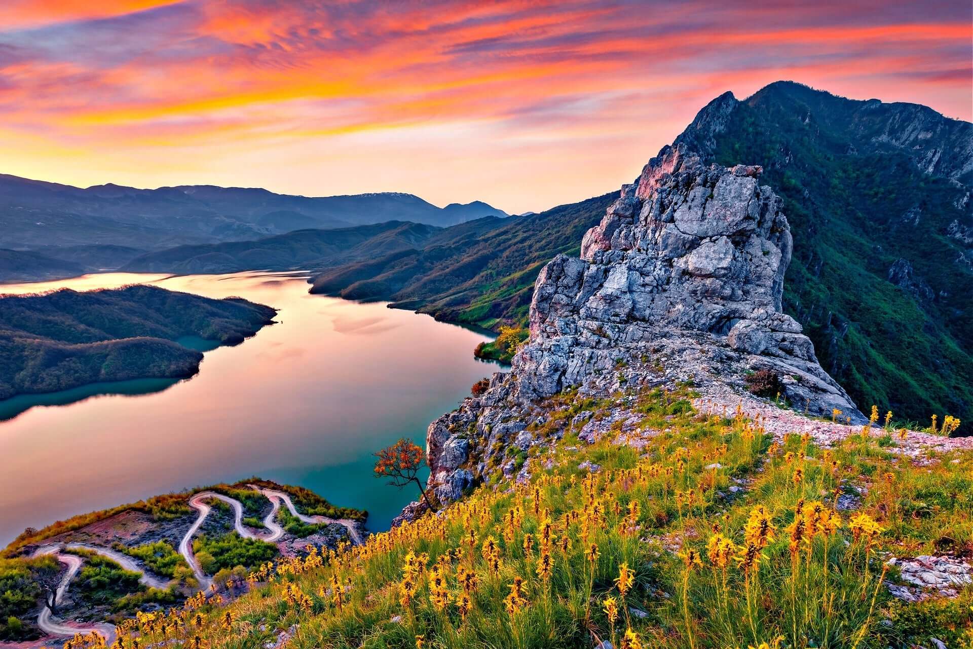 Rugged gray rock formation on Albanian grassy hillside with yellow wildflowers at sunset