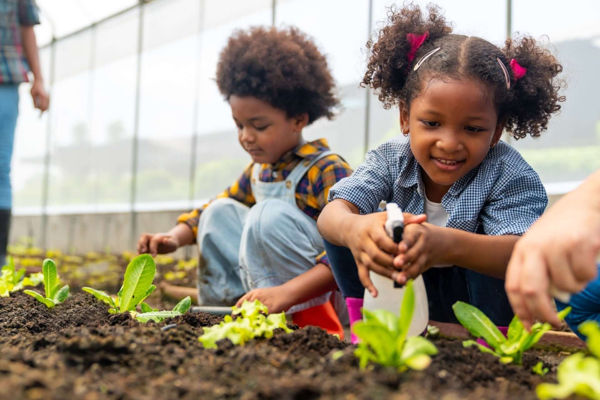 Young girl with pigtails sprays plants while gardening with children