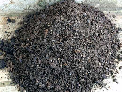 Dark brown chunky compost pile with organic debris in soil quality article