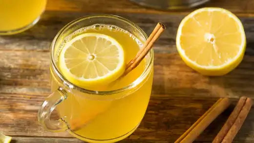 Golden lemon-infused herbal remedy in clear glass mug with lemon slice and cinnamon stick