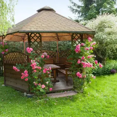 Wooden gazebo with thatched roof and pink roses in garden