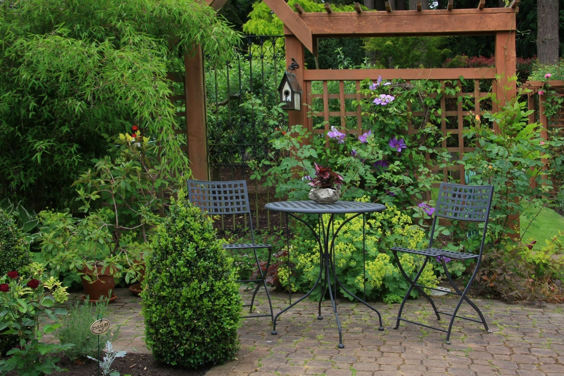 Black wrought iron patio table with round textured top in trellis garden
