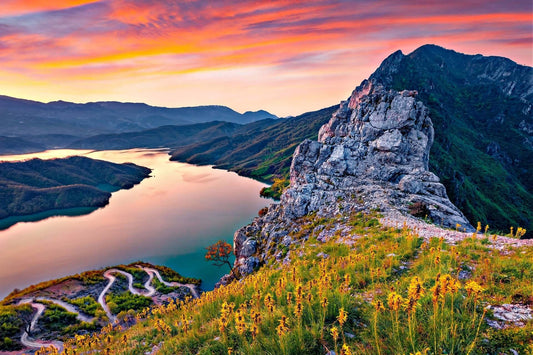 Rugged gray rock formation on Albanian grassy hillside with yellow wildflowers at sunset
