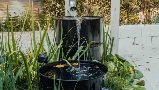 Black metal rain barrel water feature with cascading stream and leaves