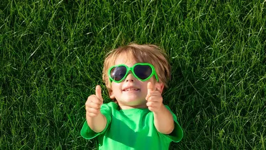 Cheerful toddler in green shirt and lime sunglasses on healthy lawn