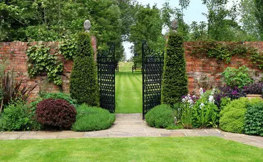 Black wrought iron gate amid manicured hedges and brick walls