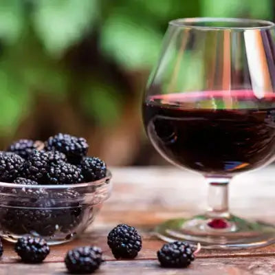 Glass snifter of dark red blackberry wine with blackberries on wood