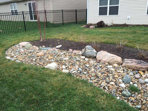 Curved garden bed of smooth multicolored river rocks bordered by large stones